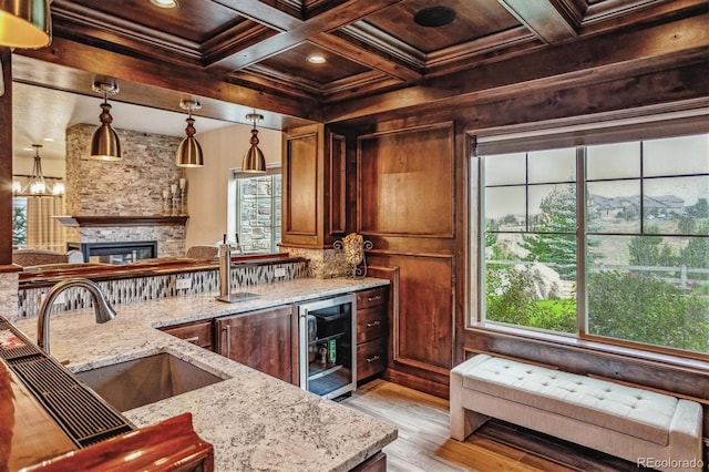 kitchen featuring a fireplace, sink, ornamental molding, beverage cooler, and light stone counters