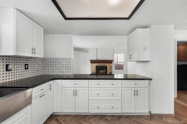 kitchen featuring white cabinets, backsplash, and a stone fireplace