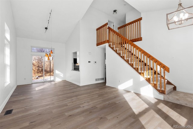 unfurnished living room featuring high vaulted ceiling, wood-type flooring, and an inviting chandelier