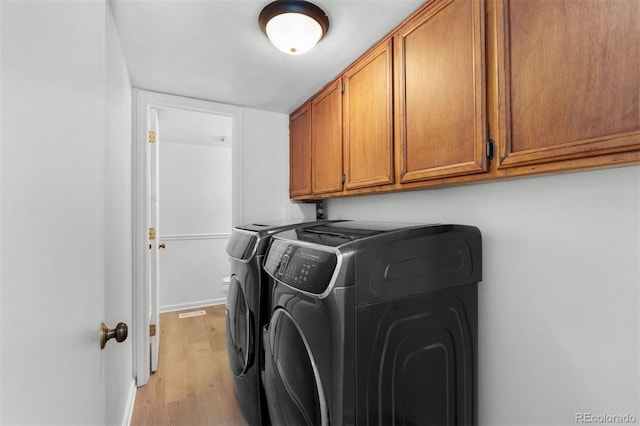 clothes washing area featuring cabinets, washer and clothes dryer, and light hardwood / wood-style floors