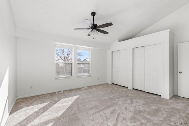 unfurnished bedroom with light carpet, two closets, ceiling fan, and lofted ceiling