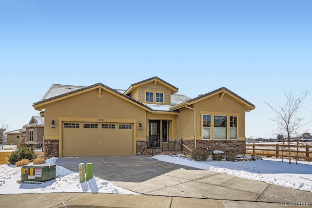 view of front of home featuring driveway, stone siding, fence, and stucco siding