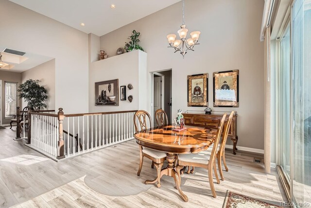 dining area featuring light wood-type flooring, visible vents, a towering ceiling, and an inviting chandelier