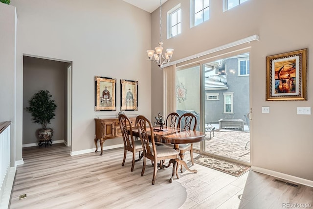 dining area with a chandelier, visible vents, a towering ceiling, and light wood finished floors