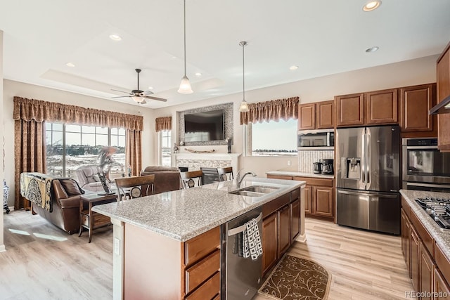 kitchen featuring a center island with sink, brown cabinetry, appliances with stainless steel finishes, open floor plan, and a sink