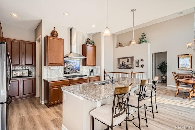 kitchen featuring a center island with sink, wall chimney exhaust hood, appliances with stainless steel finishes, hanging light fixtures, and a sink