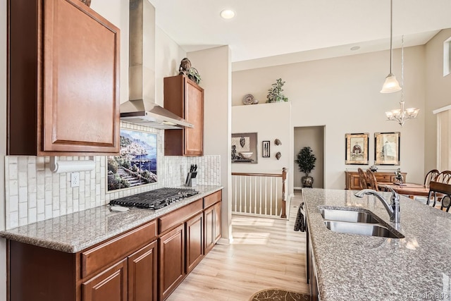 kitchen featuring stone countertops, stainless steel gas cooktop, a sink, wall chimney exhaust hood, and decorative light fixtures