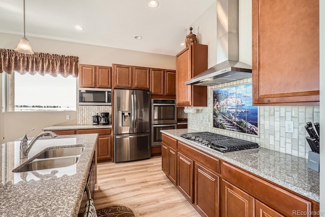 kitchen with stainless steel appliances, wall chimney range hood, a sink, and brown cabinets