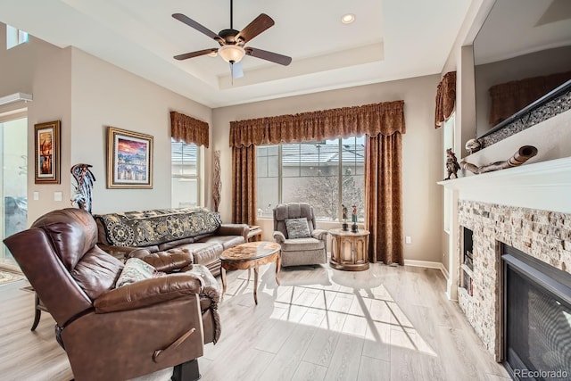 living room with light wood-type flooring, plenty of natural light, a fireplace, and a raised ceiling