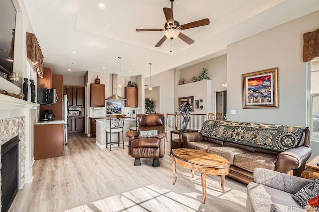 living room featuring recessed lighting, a fireplace, a ceiling fan, light wood finished floors, and a raised ceiling