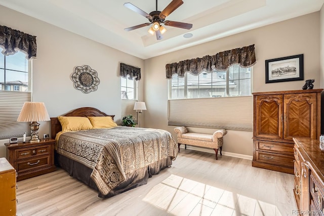 bedroom featuring a tray ceiling, baseboards, ceiling fan, and light wood finished floors