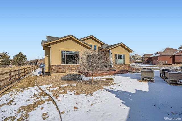 view of front of house featuring stone siding, fence, and stucco siding