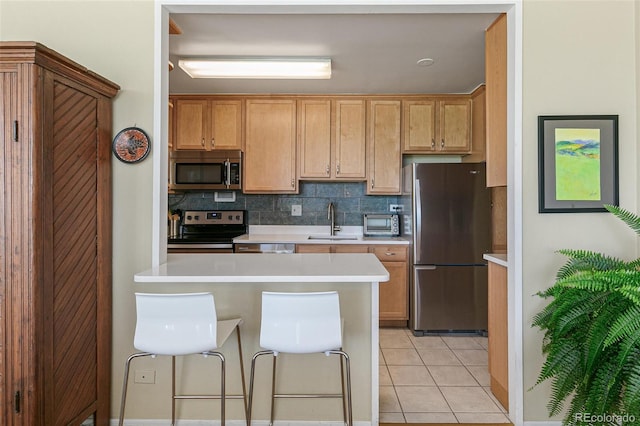 kitchen with sink, backsplash, stainless steel appliances, a kitchen breakfast bar, and light tile patterned flooring