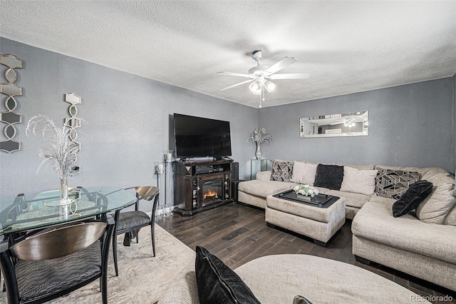 living room featuring ceiling fan, wood finished floors, a textured wall, a glass covered fireplace, and a textured ceiling