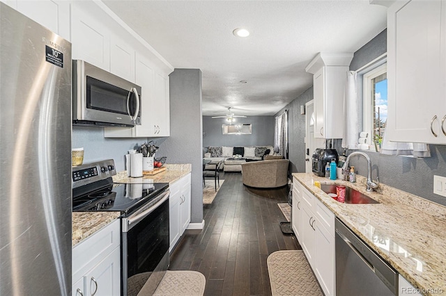 kitchen with a sink, open floor plan, appliances with stainless steel finishes, white cabinetry, and dark wood-style flooring