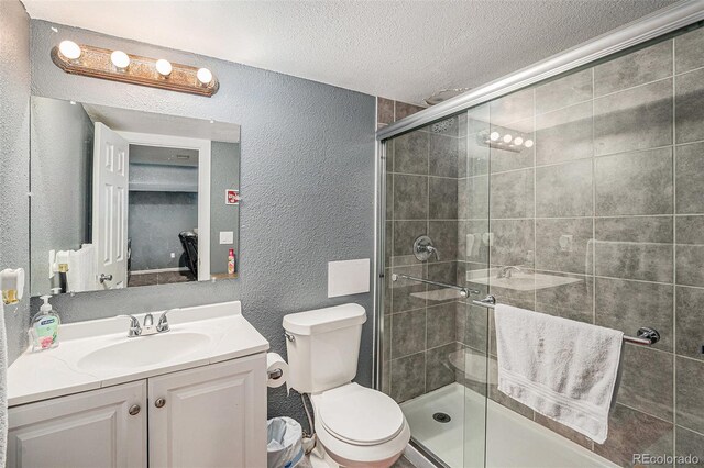 bathroom with a stall shower, a textured ceiling, vanity, and a textured wall