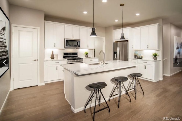 kitchen featuring white cabinets, sink, an island with sink, appliances with stainless steel finishes, and decorative light fixtures