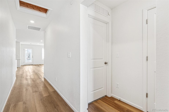 hall with light wood finished floors, attic access, and visible vents