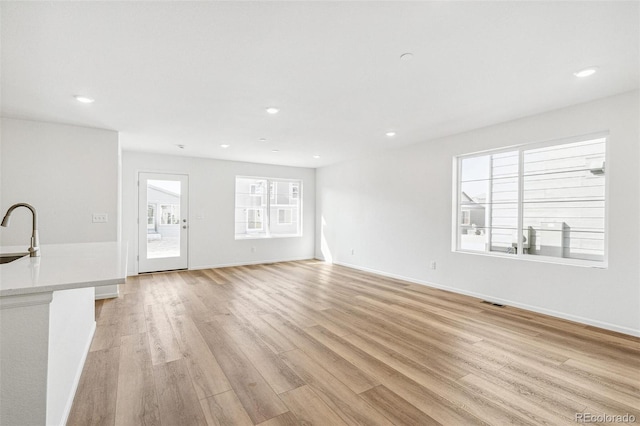 unfurnished living room with light wood-type flooring, a sink, baseboards, and recessed lighting