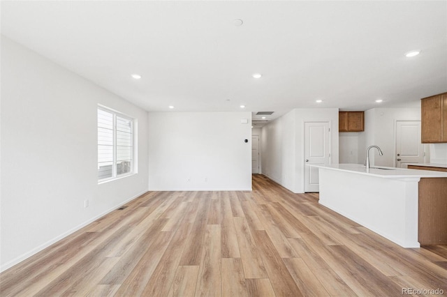 unfurnished living room featuring light wood-type flooring, visible vents, a sink, and recessed lighting