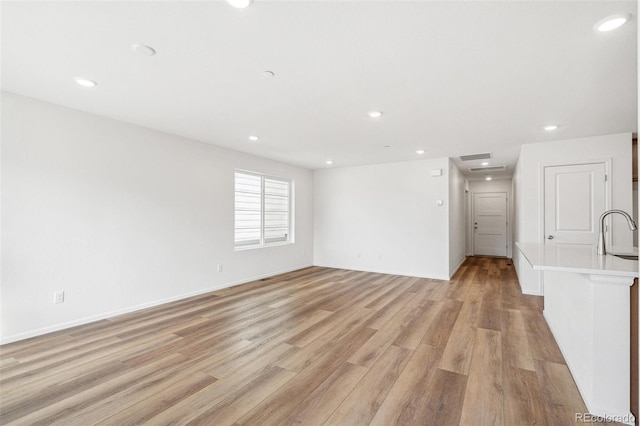 unfurnished living room with recessed lighting, a sink, and light wood-style floors