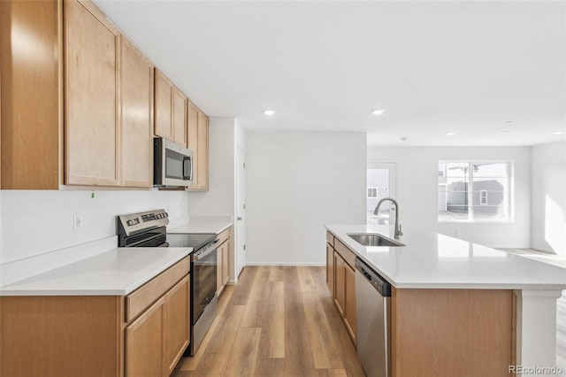 kitchen with light wood finished floors, light countertops, appliances with stainless steel finishes, a kitchen island with sink, and a sink