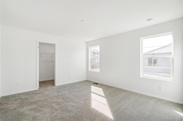 unfurnished bedroom with carpet floors, multiple windows, a walk in closet, and baseboards