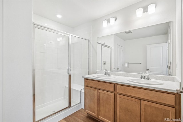 bathroom with double vanity, wood finished floors, a sink, and a shower stall