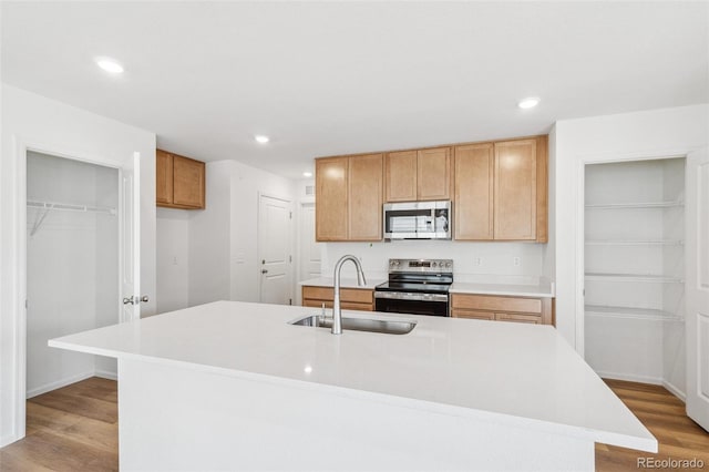 kitchen featuring a center island with sink, light countertops, appliances with stainless steel finishes, a sink, and light wood-type flooring