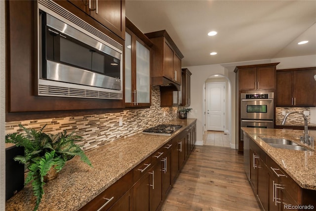 9266 E 35th Ave, Denver, CO 80238 - kitchen featuring appliances with stainless steel finishes, a sink, arched walkways, wood finished floors, and light stone counters