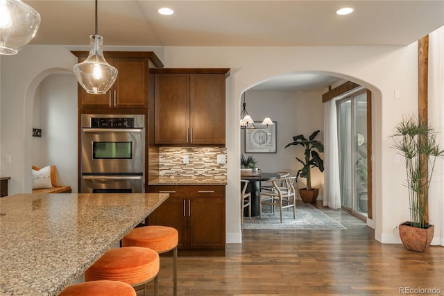 9266 E 35th Ave, Denver, CO 80238 - kitchen with arched walkways, backsplash, dark wood finished floors, light stone countertops, and a breakfast bar