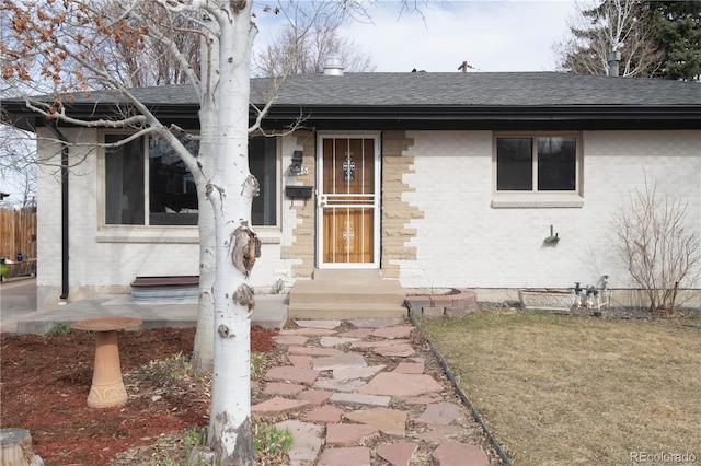 property entrance with fence, brick siding, and a shingled roof