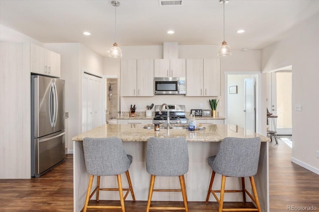 kitchen featuring pendant lighting, light stone counters, an island with sink, and appliances with stainless steel finishes