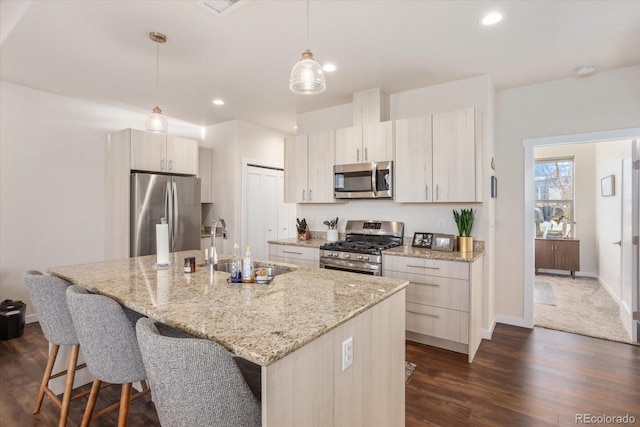 kitchen with pendant lighting, sink, stainless steel appliances, light stone counters, and a center island with sink