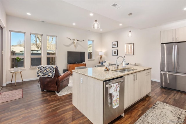 kitchen with sink, pendant lighting, stainless steel appliances, light stone countertops, and a kitchen island with sink