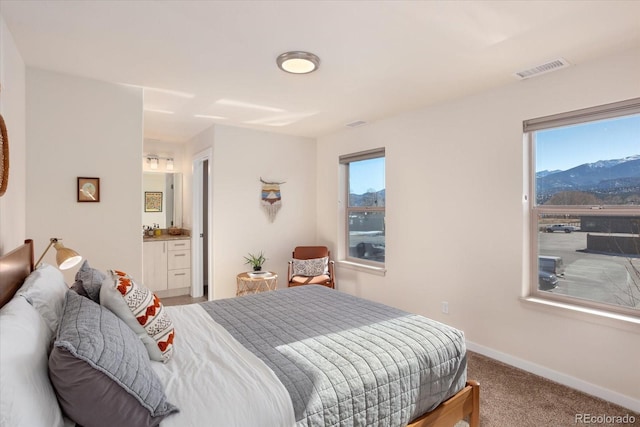 carpeted bedroom featuring connected bathroom, a mountain view, and multiple windows