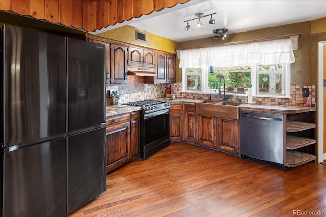 kitchen featuring sink, tasteful backsplash, hardwood / wood-style floors, dark brown cabinets, and black appliances