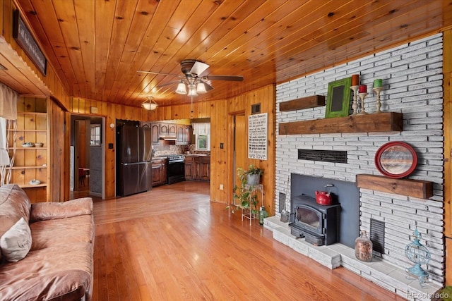 living room with light hardwood / wood-style flooring, a wood stove, and ceiling fan