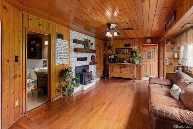 living room with wooden ceiling, a wood stove, wooden walls, light hardwood / wood-style flooring, and ceiling fan