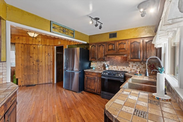 kitchen featuring tasteful backsplash, stainless steel fridge, tile counters, and black range