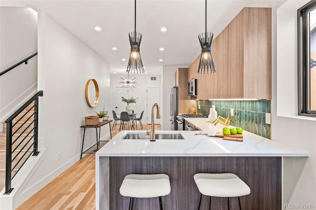 kitchen featuring pendant lighting, sink, backsplash, premium appliances, and light stone countertops