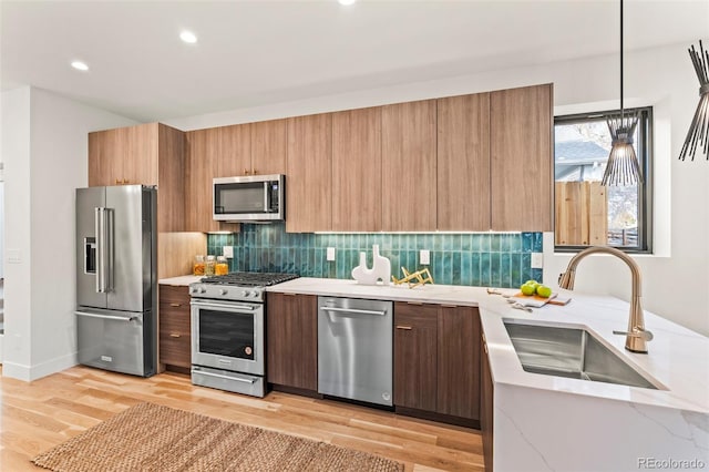 kitchen with pendant lighting, sink, backsplash, stainless steel appliances, and light hardwood / wood-style floors