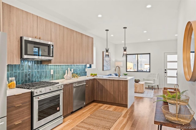 kitchen with appliances with stainless steel finishes, decorative light fixtures, sink, light hardwood / wood-style floors, and kitchen peninsula