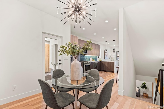 dining area featuring sink, a chandelier, and light wood-type flooring