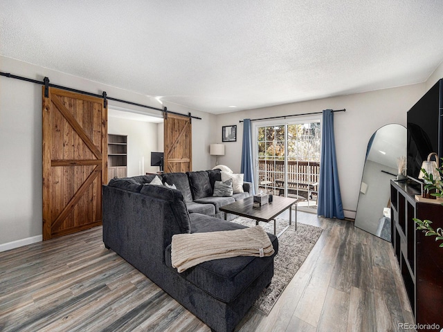 living area with a barn door, a textured ceiling, baseboards, and wood finished floors