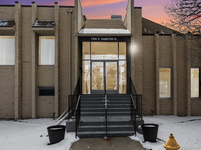 snow covered property entrance with french doors and a shingled roof