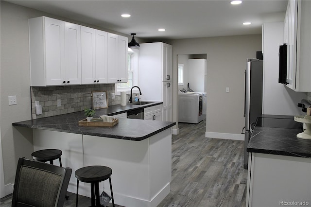 kitchen featuring light hardwood / wood-style flooring, washing machine and clothes dryer, kitchen peninsula, sink, and white cabinets