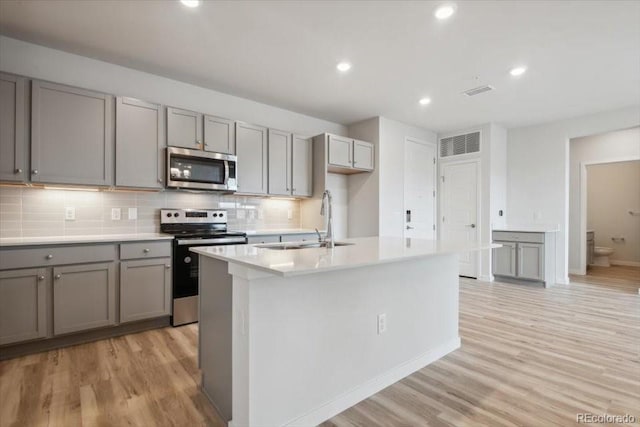 kitchen featuring gray cabinets, sink, light wood-type flooring, a kitchen island with sink, and appliances with stainless steel finishes