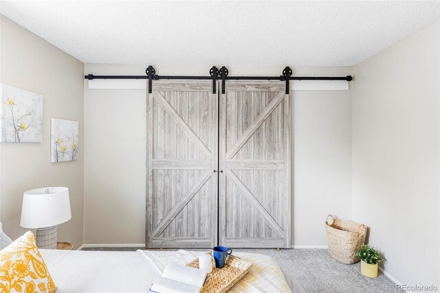 carpeted bedroom with a barn door, a textured ceiling, and baseboards