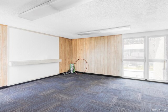 spare room with carpet floors, wooden walls, baseboards, and a textured ceiling